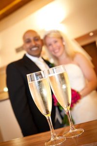 Champagne in the foreground with bride and groom smiling in the background